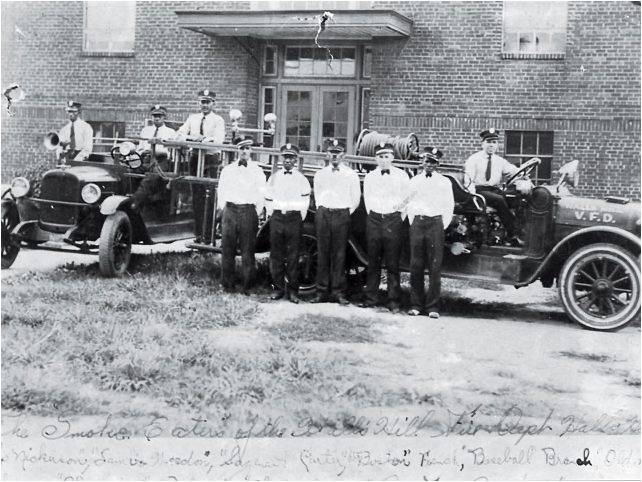 Photo of 8 uniformed firefighters with two pieces of fire apparatus.