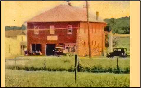 Cherrydale fire house pictured in the 1920's. Two story red brick fire station adjoining a white single story structure and otherwise surrounded by fields. Two cars are parked by the fire station.